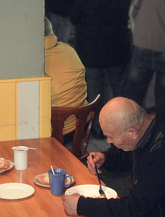 älterer mann sitzt in einer suppenküche am tisch und isst