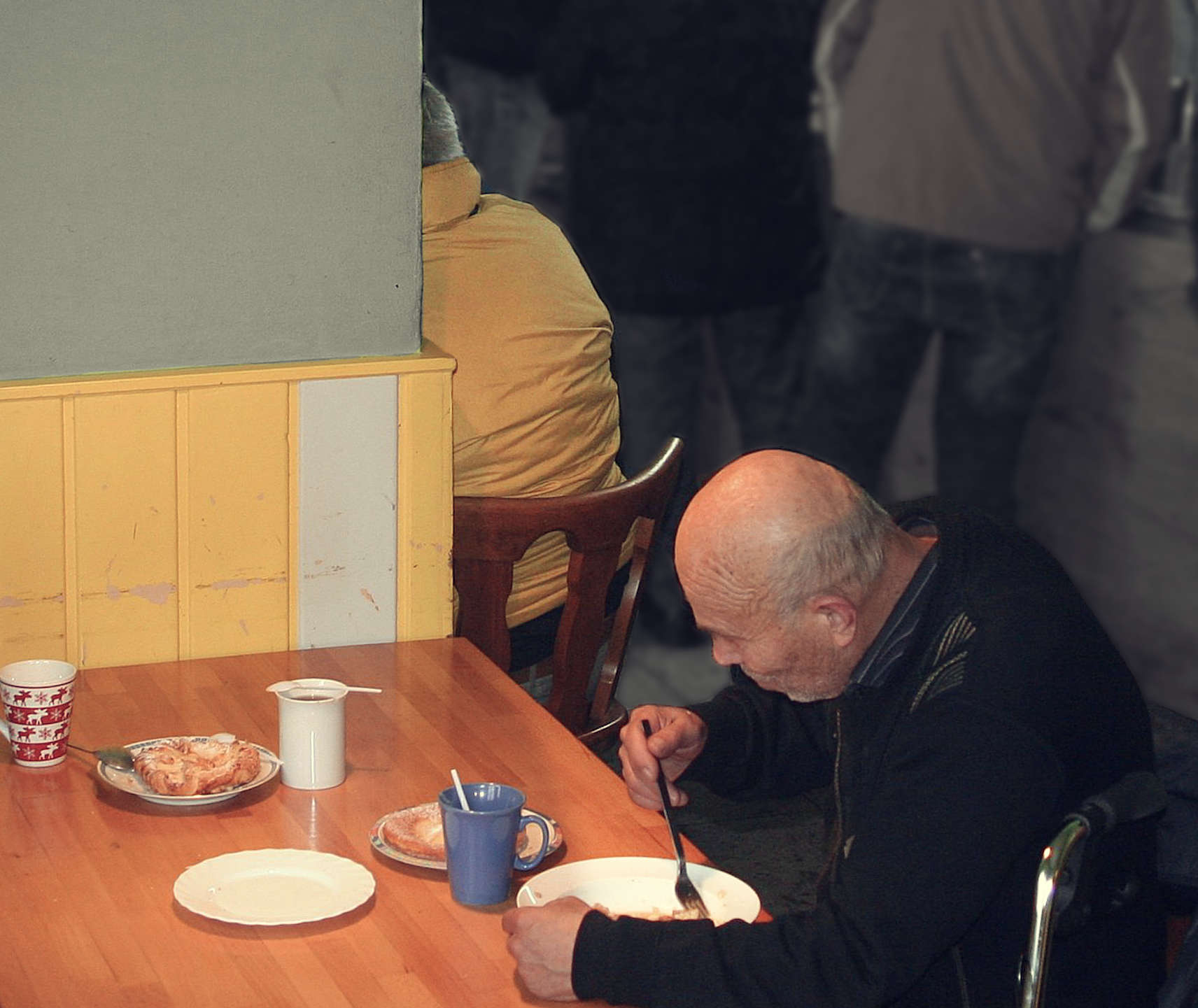 älterer mann sitzt in einer suppenküche am tisch und isst