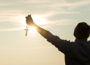 Junger Mann hält Kreuz in die Sonne