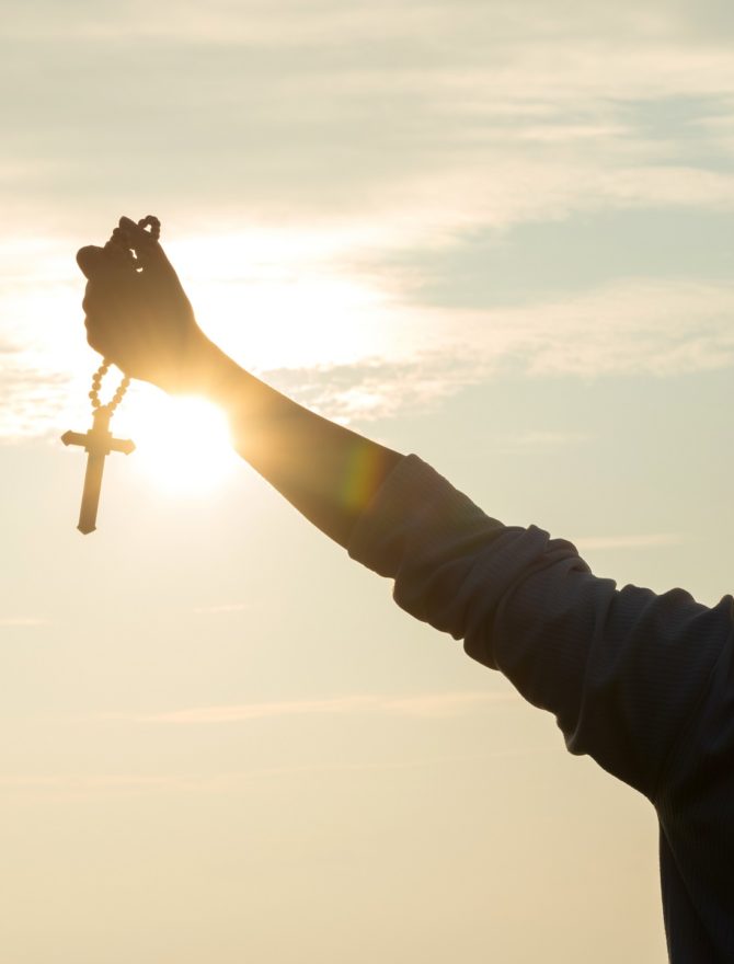 Junger Mann hält Kreuz in die Sonne