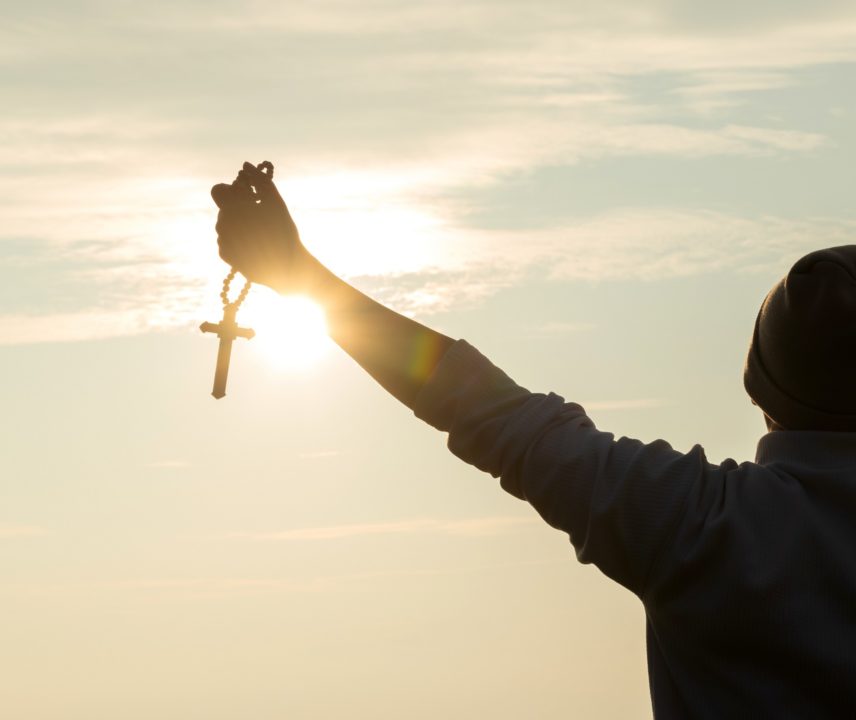 Junger Mann hält Kreuz in die Sonne