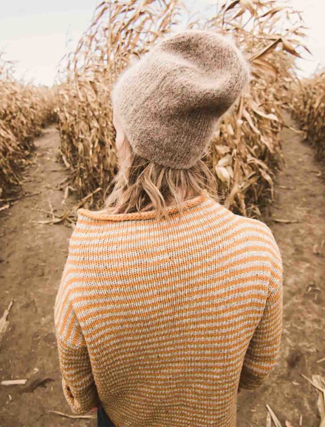 junge Blonde Frau steht in einem Maisfeld vor einer Weggabelung
