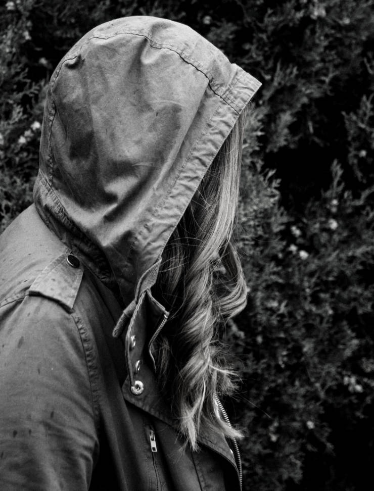 Symbolbild in schwarz-weiss: junge Frau bei Regen im Parker. Das Gesicht ist durch die Kapuze verdeckt.