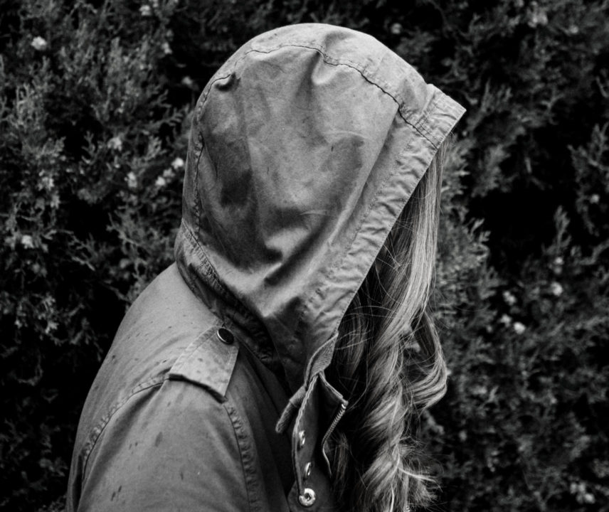 Symbolbild in schwarz-weiss: junge Frau bei Regen im Parker. Das Gesicht ist durch die Kapuze verdeckt.