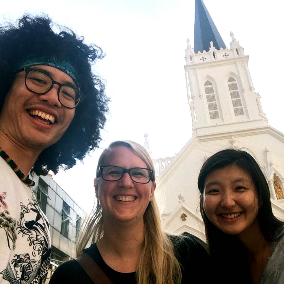 Zwei junge Frauen und ein junger Mann vor einer Kirche.