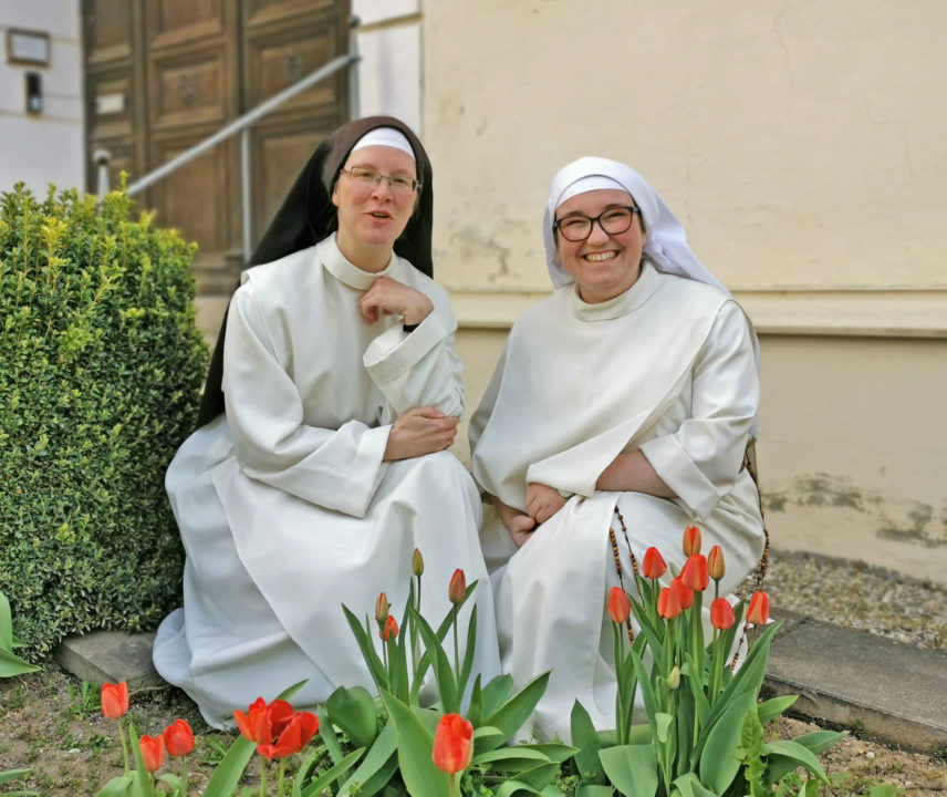 Zwei junge Dominikanerinnen in weißer Ordenstracht im Garten mit roten Tulpen