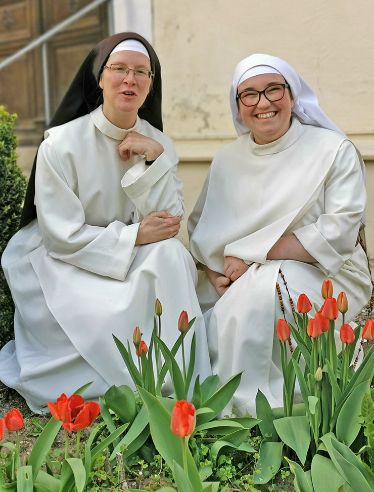 Zwei junge Dominikanerinnen in weißer Ordenstracht im Garten mit roten Tulpen