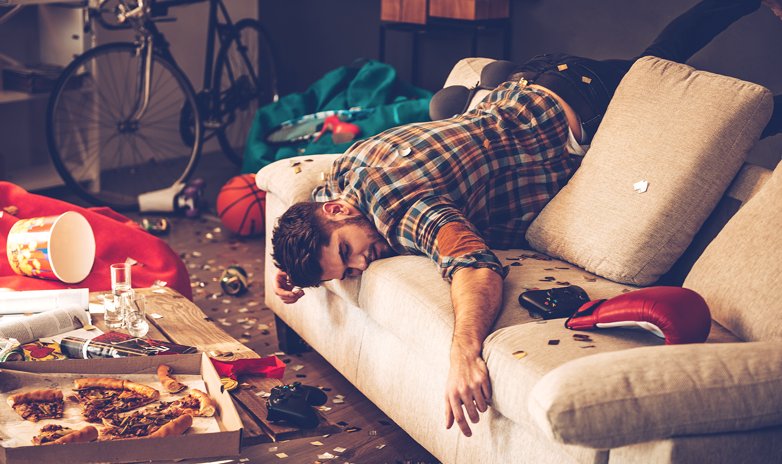 Junger Mann liegt erschöpft nach der Party schlafend auf der Couch.