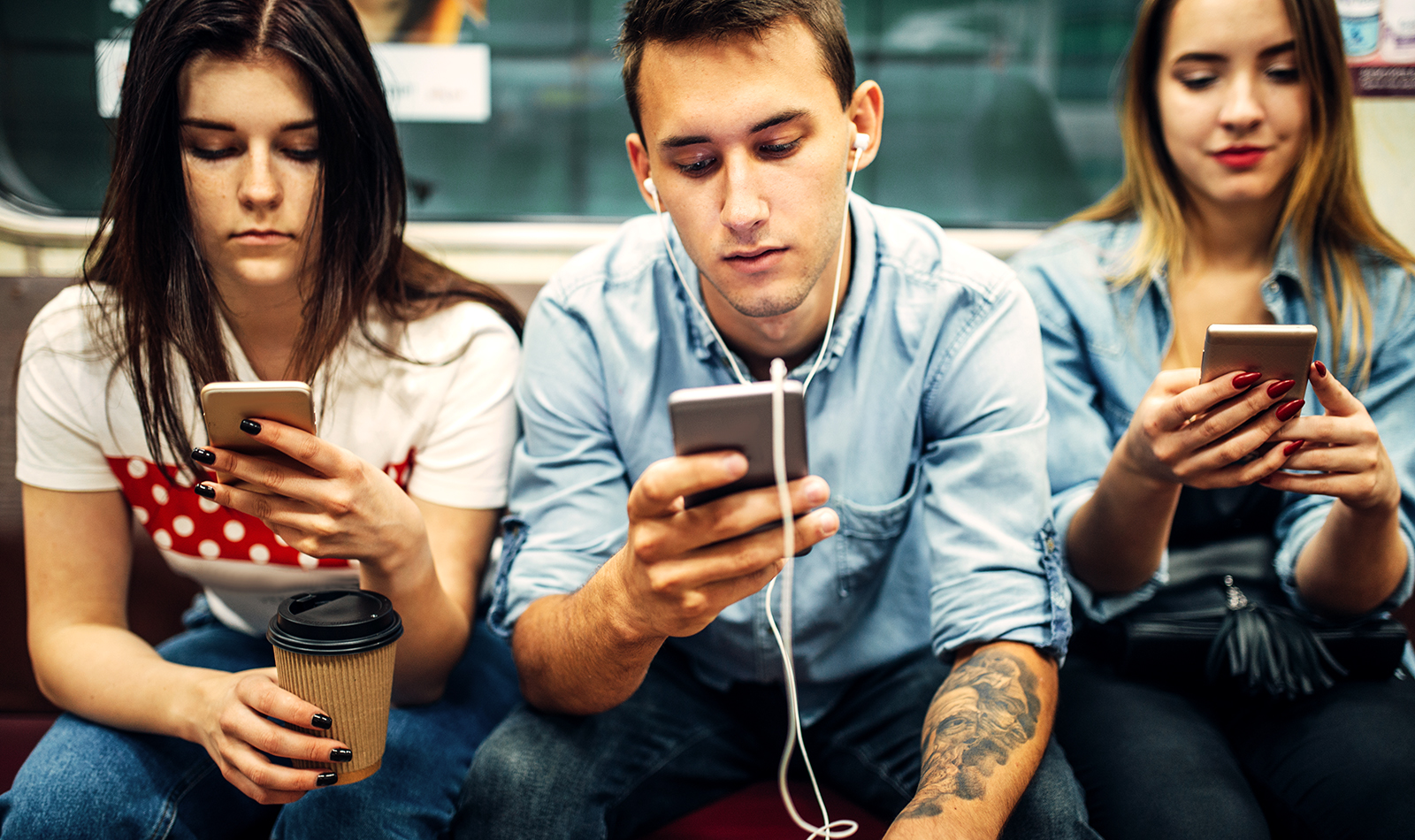 Junge Erwachsene in der U-Bahn blicken auf ihr Smartphone