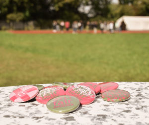 Buttons mit der Aufschrift "WELTfairÄNDERER", im Hintergrund eine Schulklasse auf einer Wiese