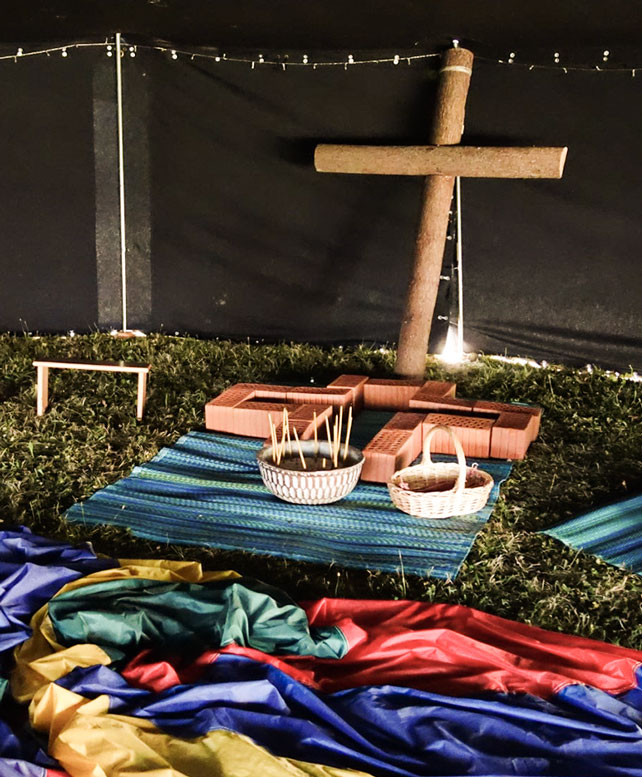 Dunkles Zelt mit einem Holzkreuz und bunten Tüchern