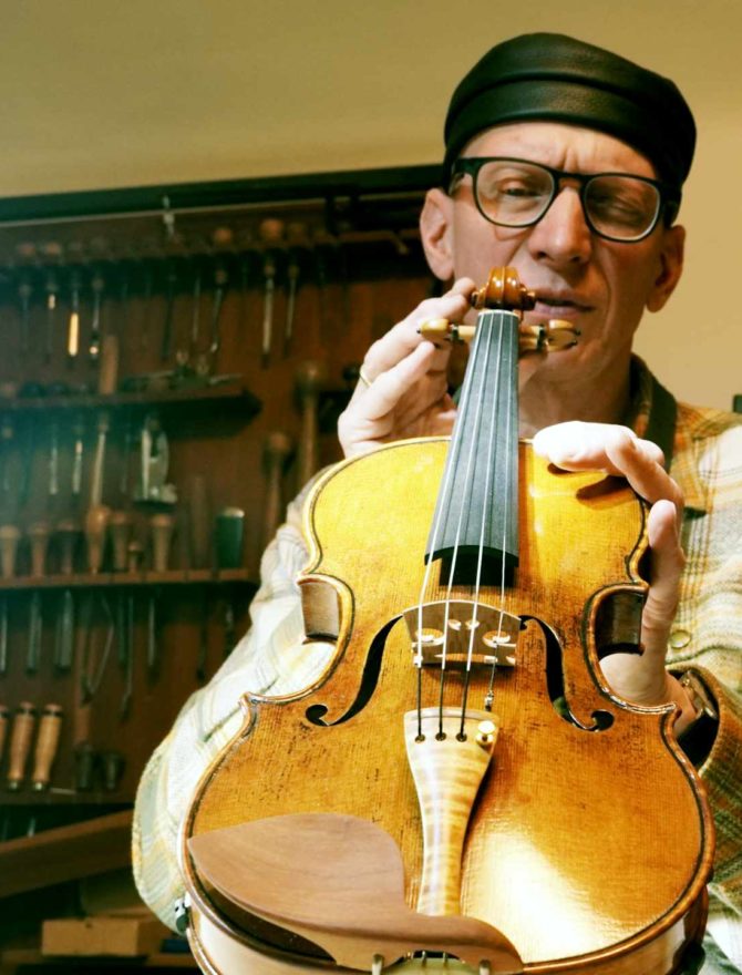 Geigenbauer mit Geige in seiner Werkstatt