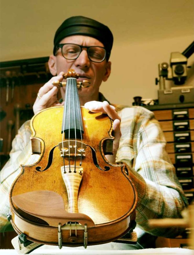 Geigenbauer mit Geige in seiner Werkstatt