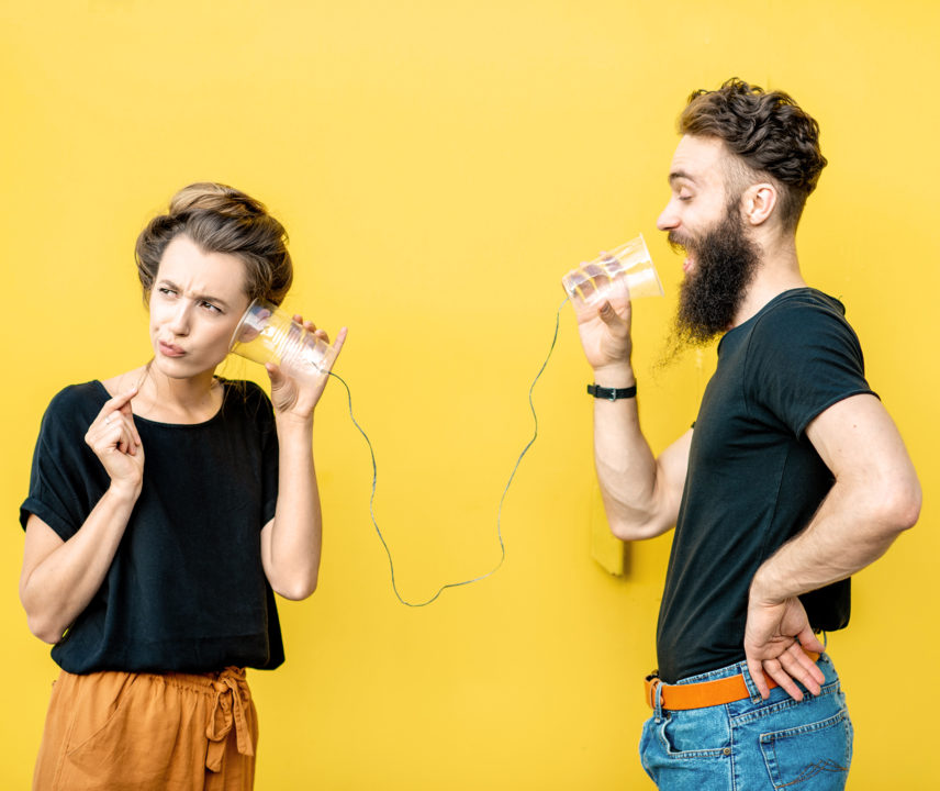 Junge Frau und junger Mann versuchen mit Bechern und Schnur zu kommunizieren