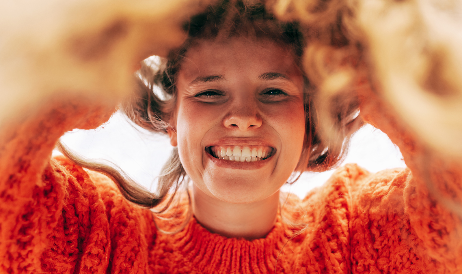 Junge Frau mit breitem lachen in gestricktem orangen Pullover blickt direkt von oben in die Kamera