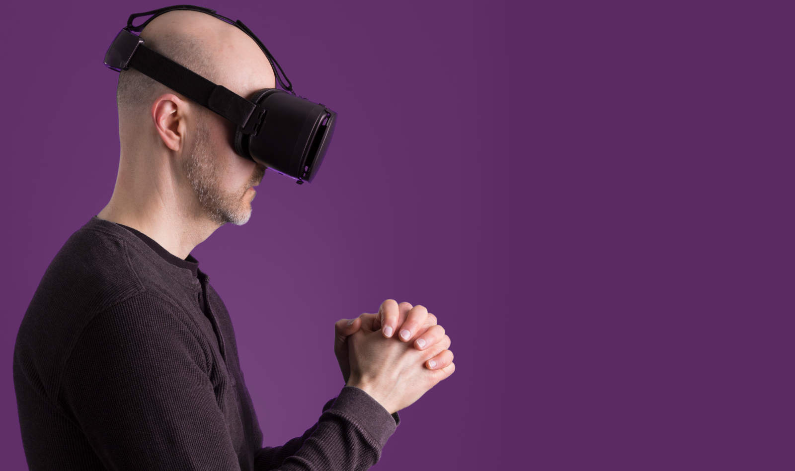 Junger europäischer Mann mit Glatze beim Gebet mit einem Virtual Reality Headset Kopfhörer
