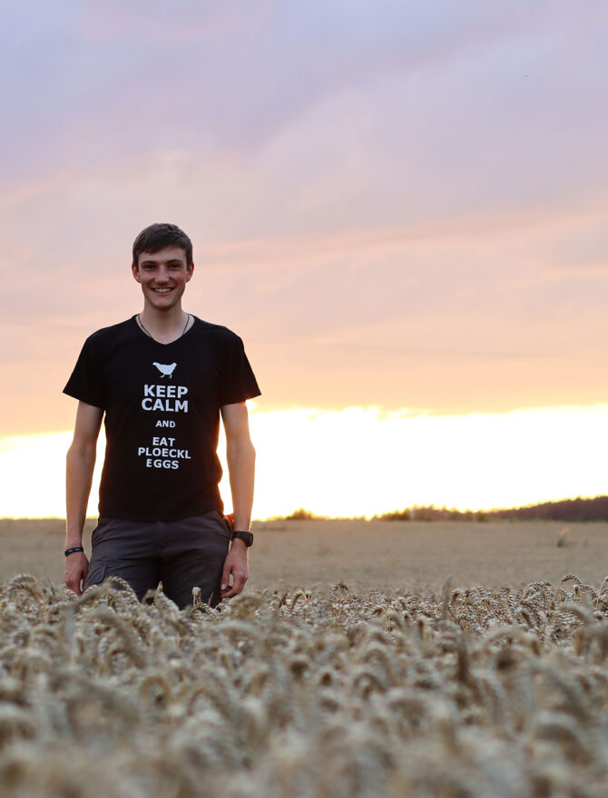 Junger Mann in schwarzem T-Shirt läuft glücklich bei Sonnenuntergang über ein Weizenfeld