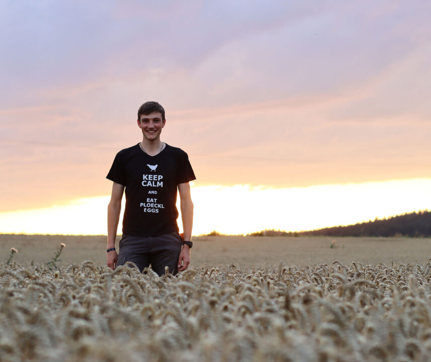 Junger Mann in schwarzem T-Shirt läuft glücklich bei Sonnenuntergang über ein Weizenfeld