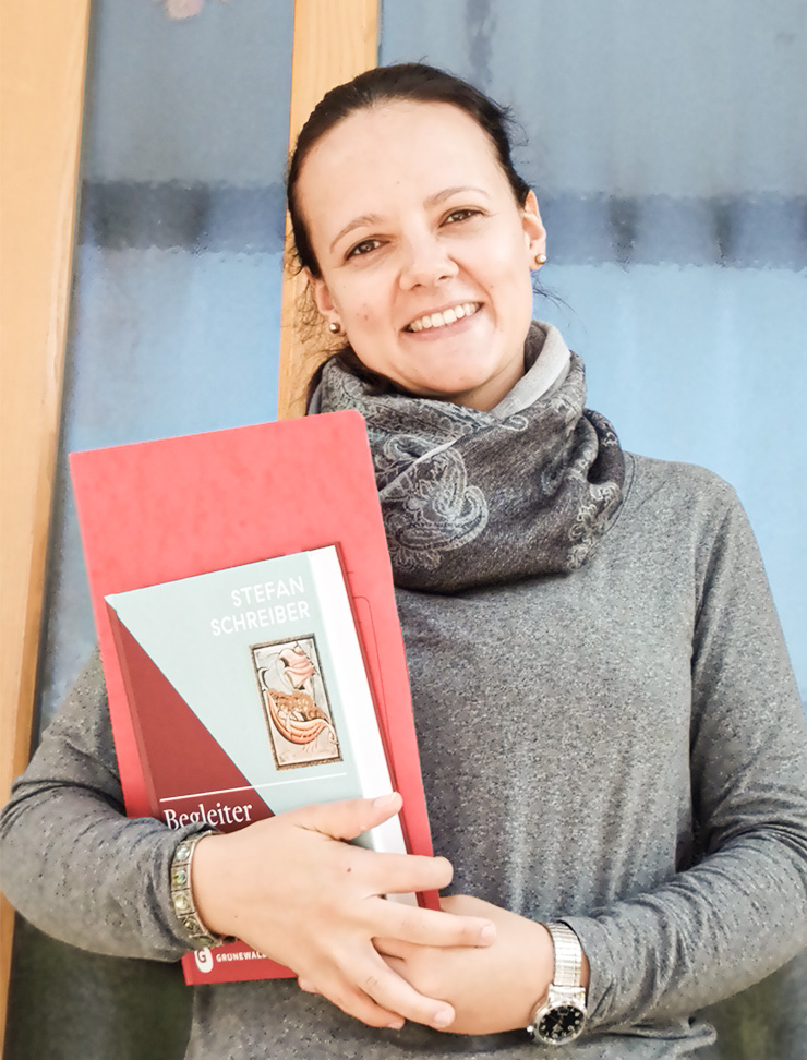 Junge europäische Frau mit schwarzen Haaren und Studienmaterial Theologie vor einem Fenster