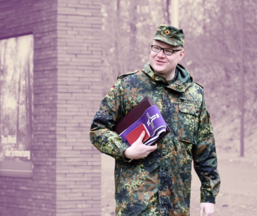 Etwas kräftigerer deutscher Bundeswehrsoldat in Uniform und Brille mit lila Buch für Seelsorge unter dem Arm