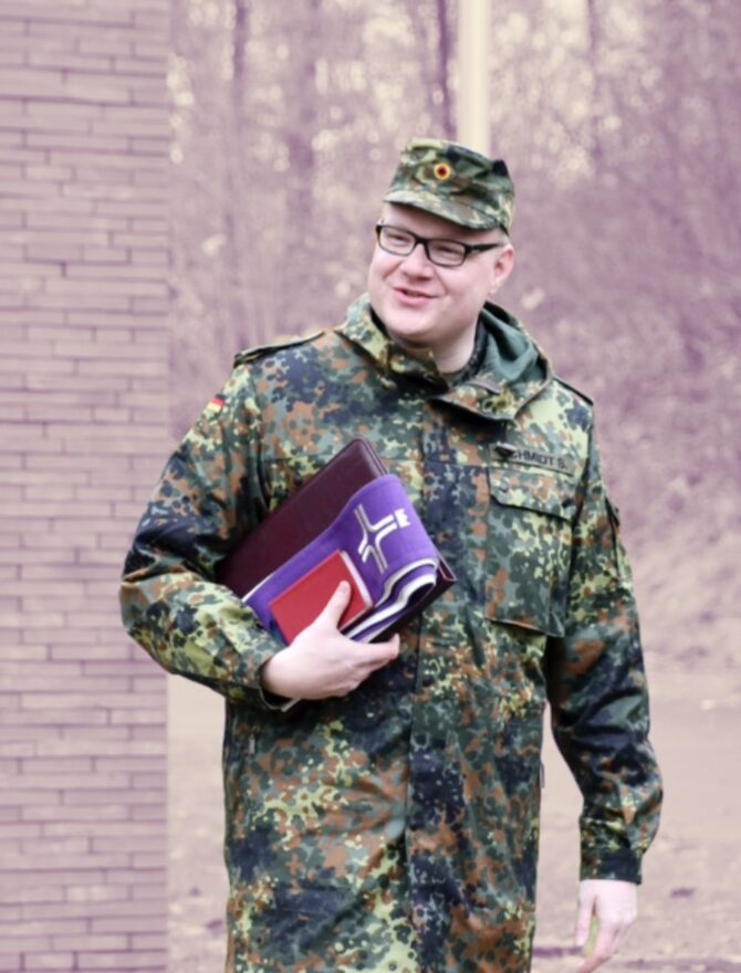 Etwas kräftigerer deutscher Bundeswehrsoldat in Uniform und Brille mit lila Buch für Seelsorge unter dem Arm