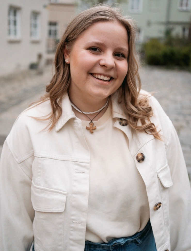 Porträt einder jungen europäischen Frau mit langen blonden gelockten Haaren, lachend mit Holzkreuzkette, weißer Kette, Ohrringen in weißem Shirt und weißem Hemd