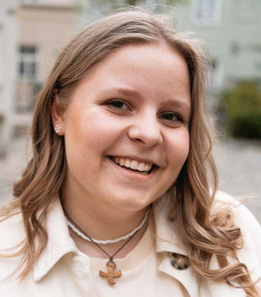 Porträt einder jungen europäischen Frau mit langen blonden gelockten Haaren, lachend mit Holzkreuzkette, weißer Kette, Ohrringen in weißem Shirt und weißem Hemd